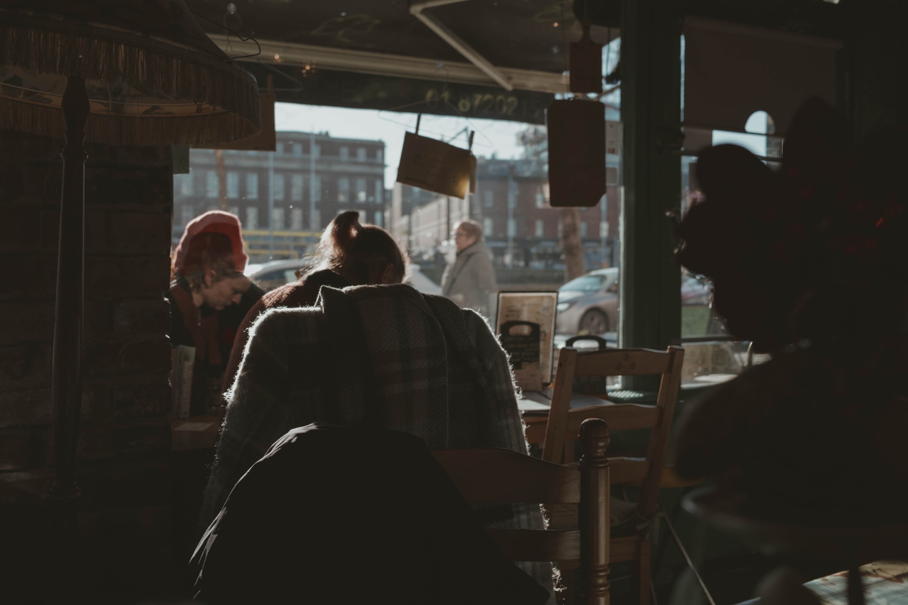Woman sitting quietly in a cafe while people pass by outside.
