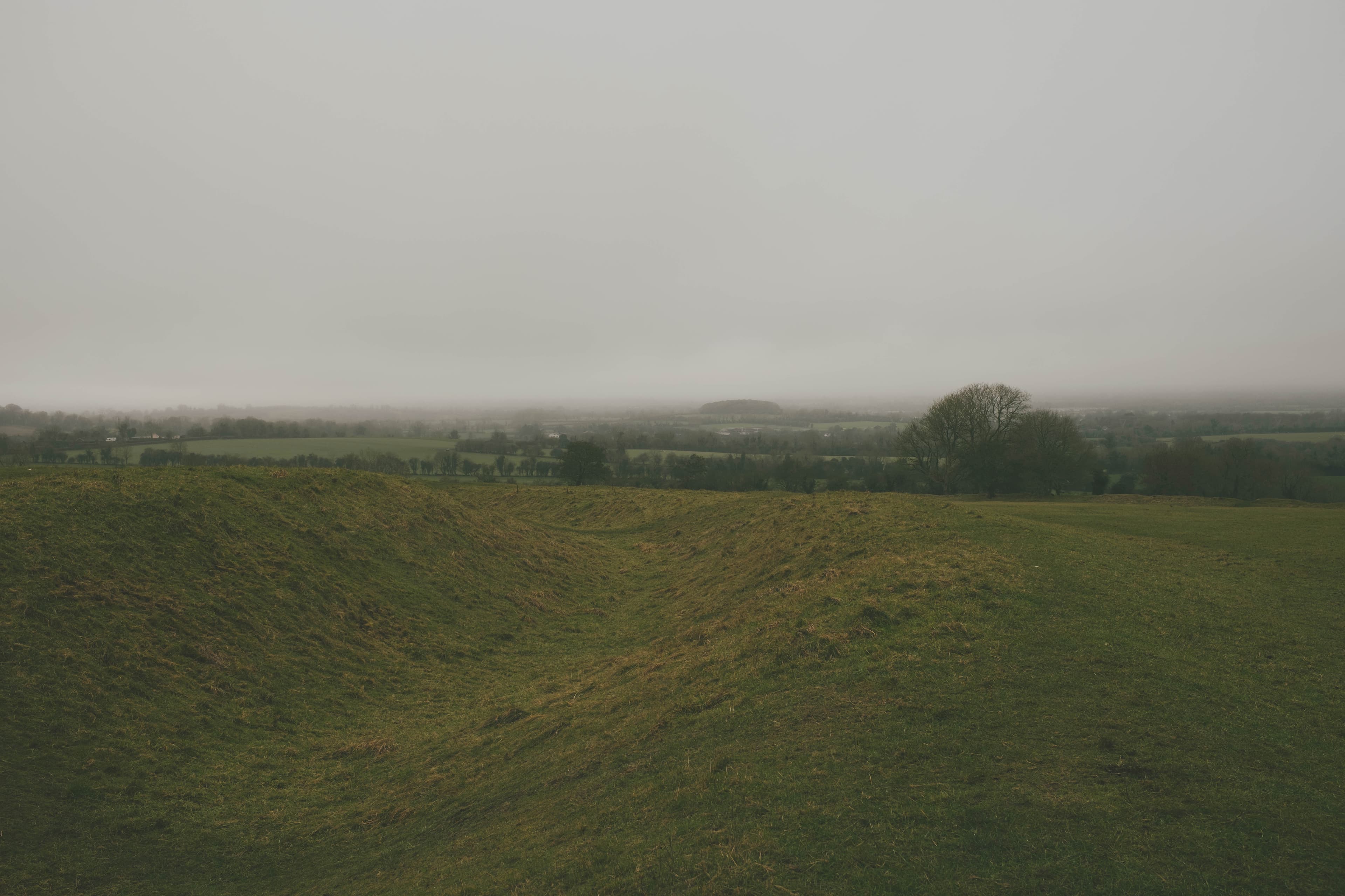 A grave stone with celtic cross in a large, empty field on a foggy day.