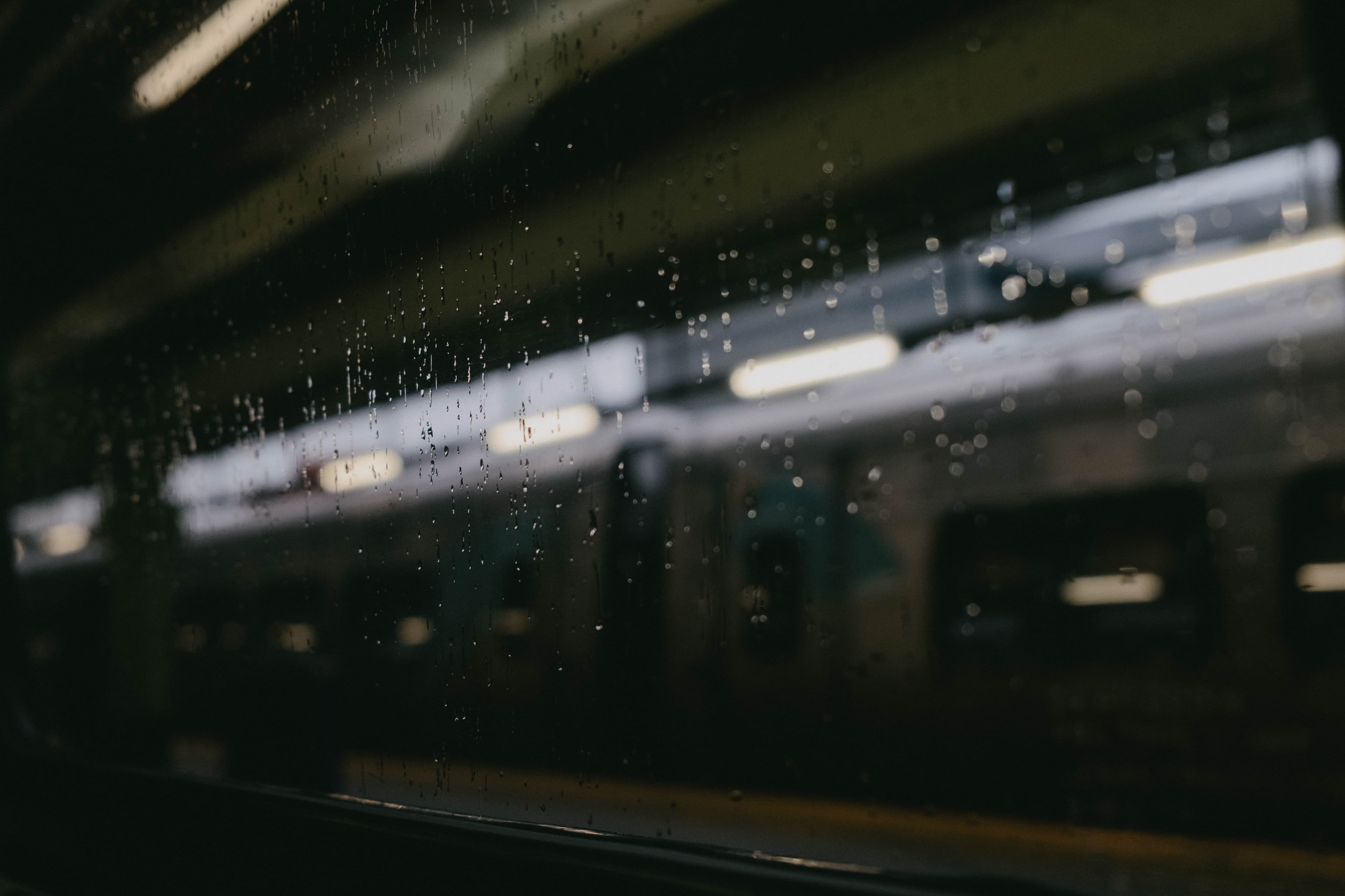 Shallow depth of field from inside a train, looking out the window. Streaks of rain are in focus while everthing else outside the window is blurred.