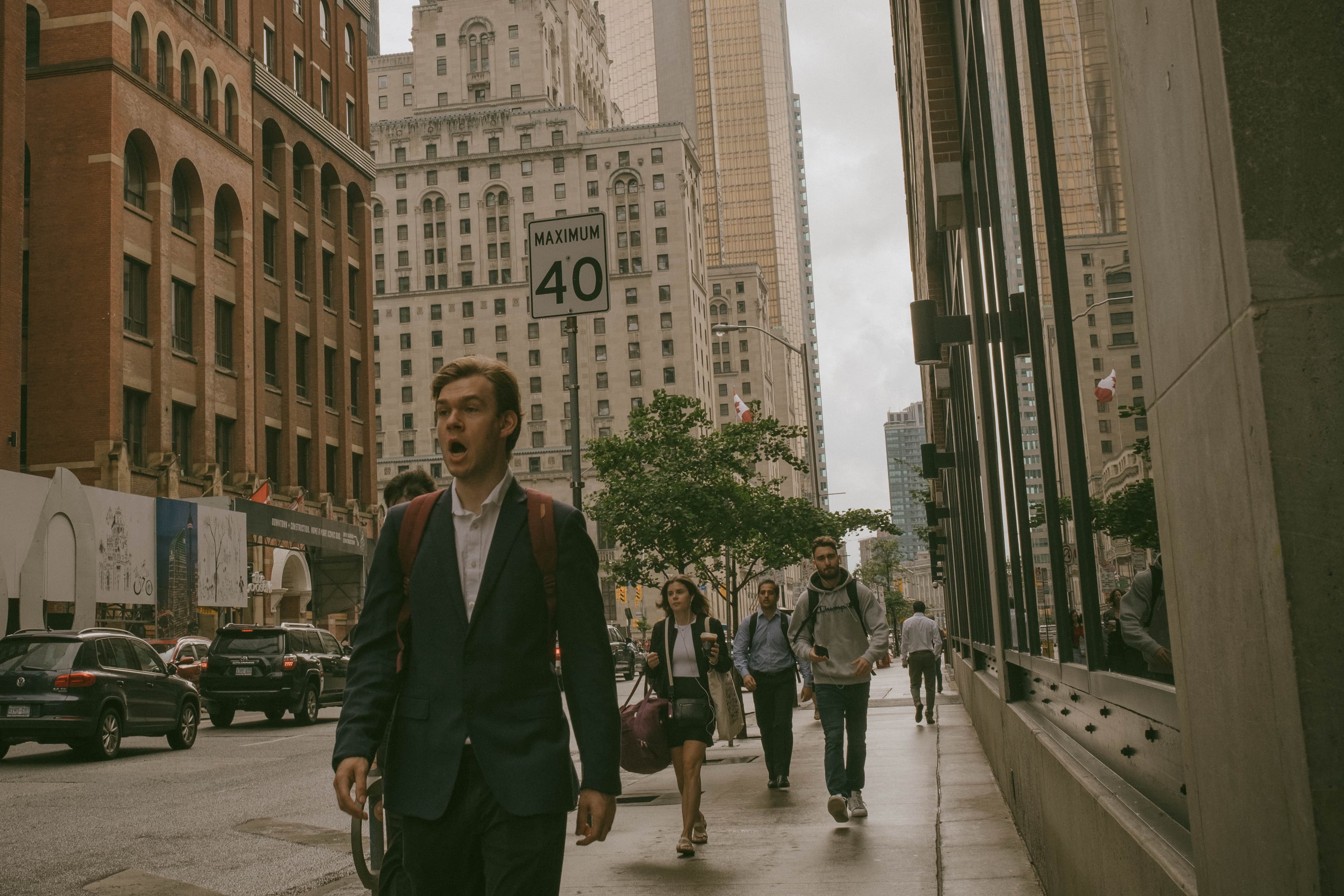 Pedestrians walking a city street. One person appears to be yawning.