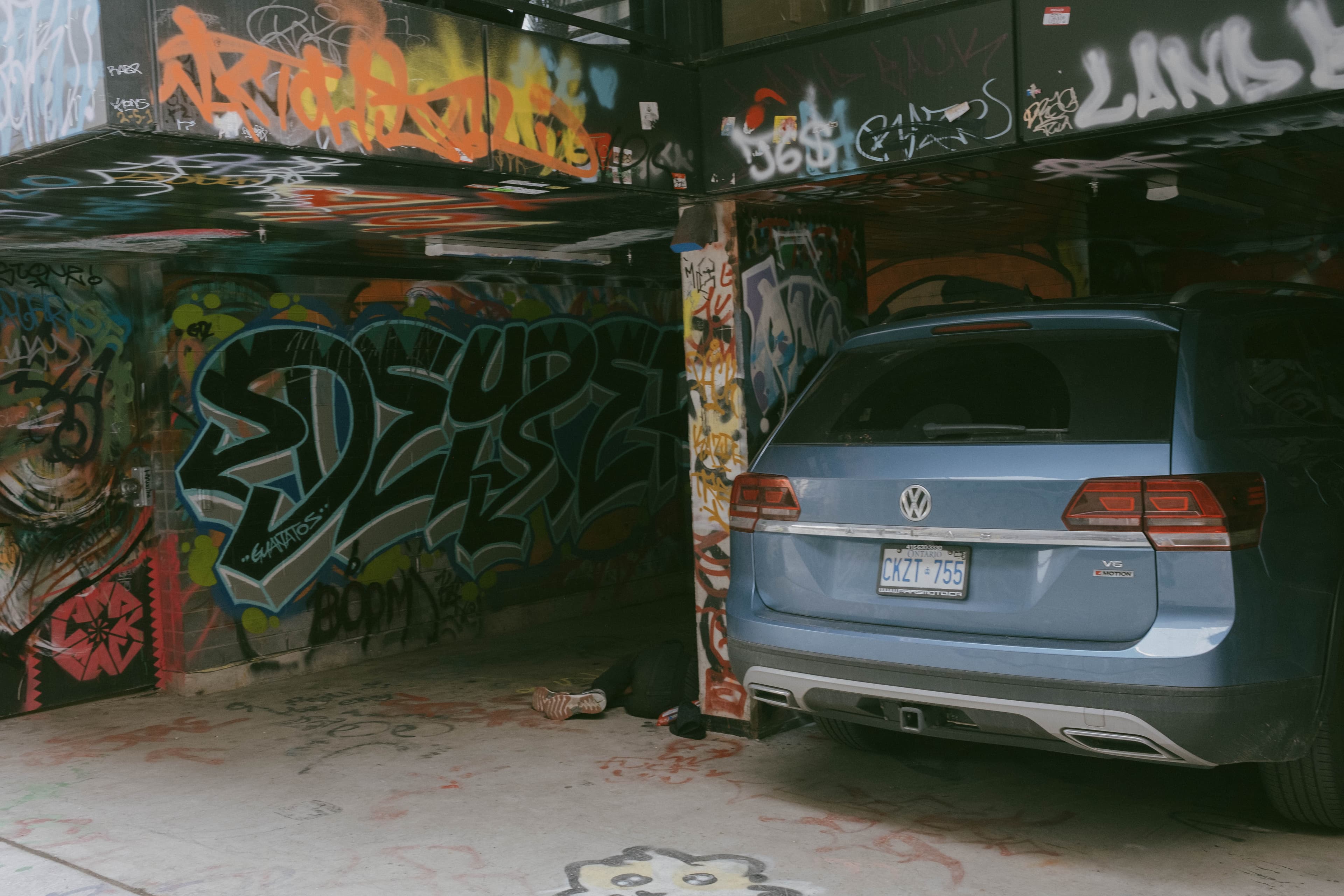 Legs coming from out of the shadow where someone appears passed out. Heavily spray painted garage.