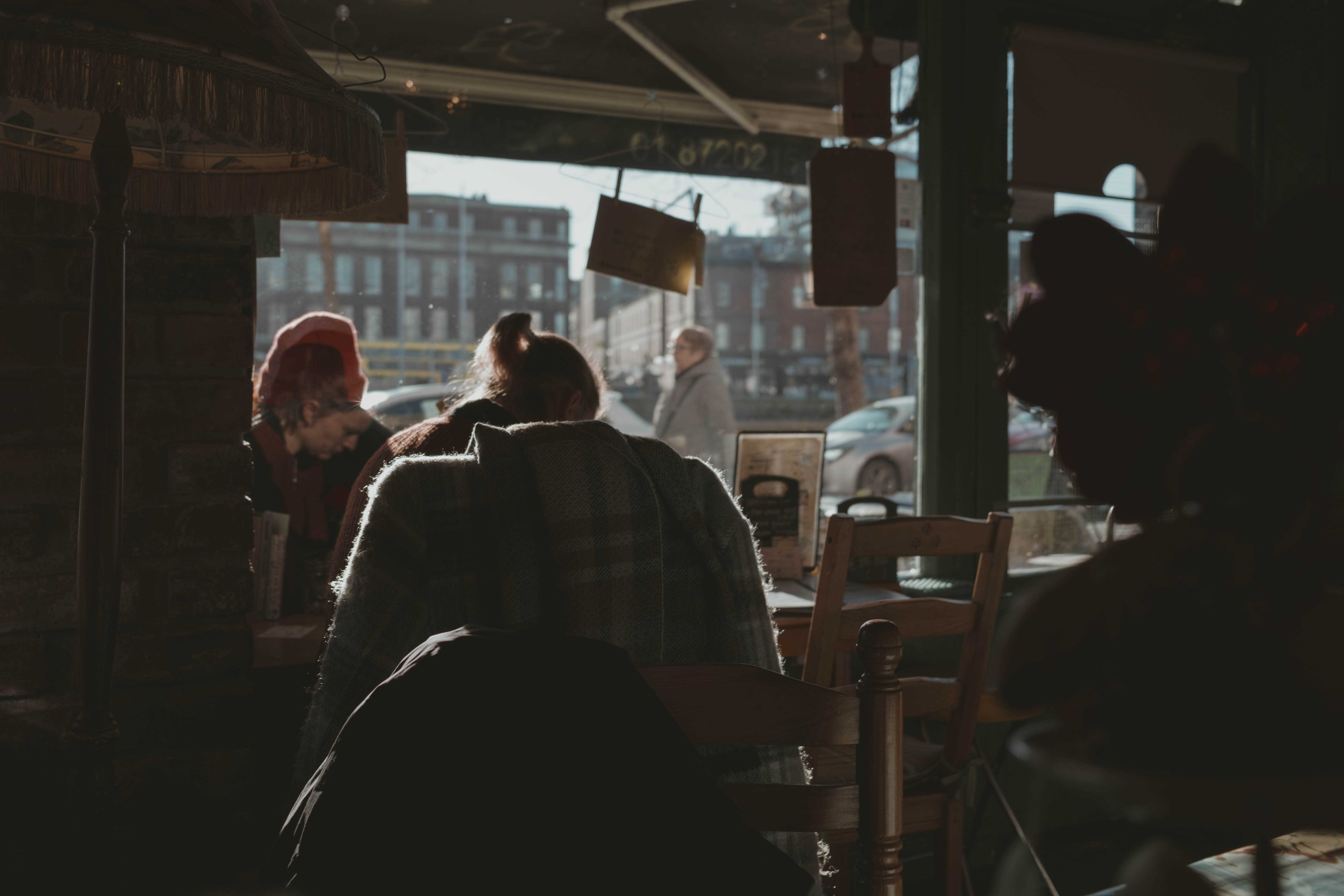 Woman sitting quietly in a cafe while people pass by outside.