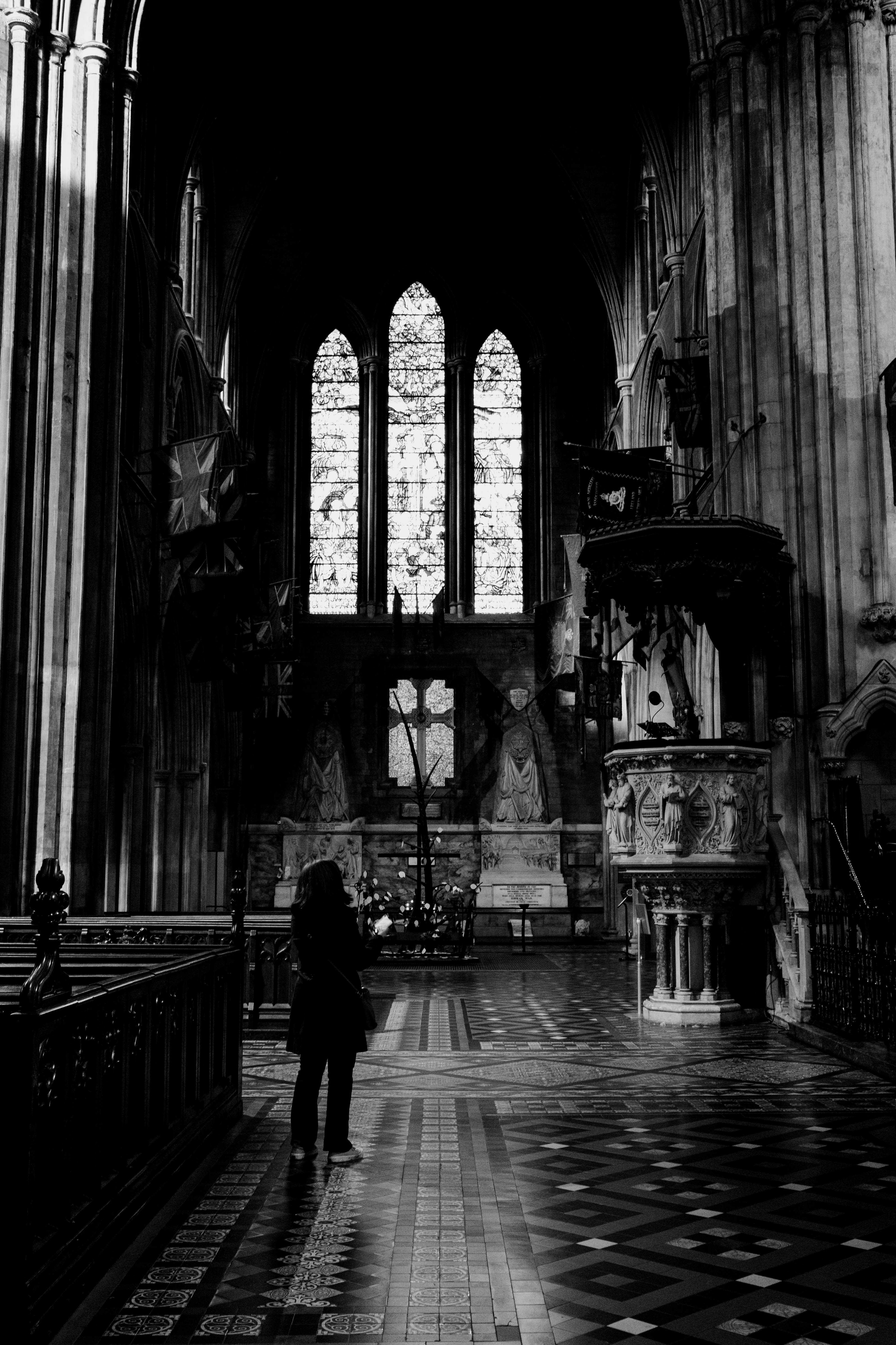 A person looking up at the pulpit, situated across from them. The stained glass windows are high up in the background