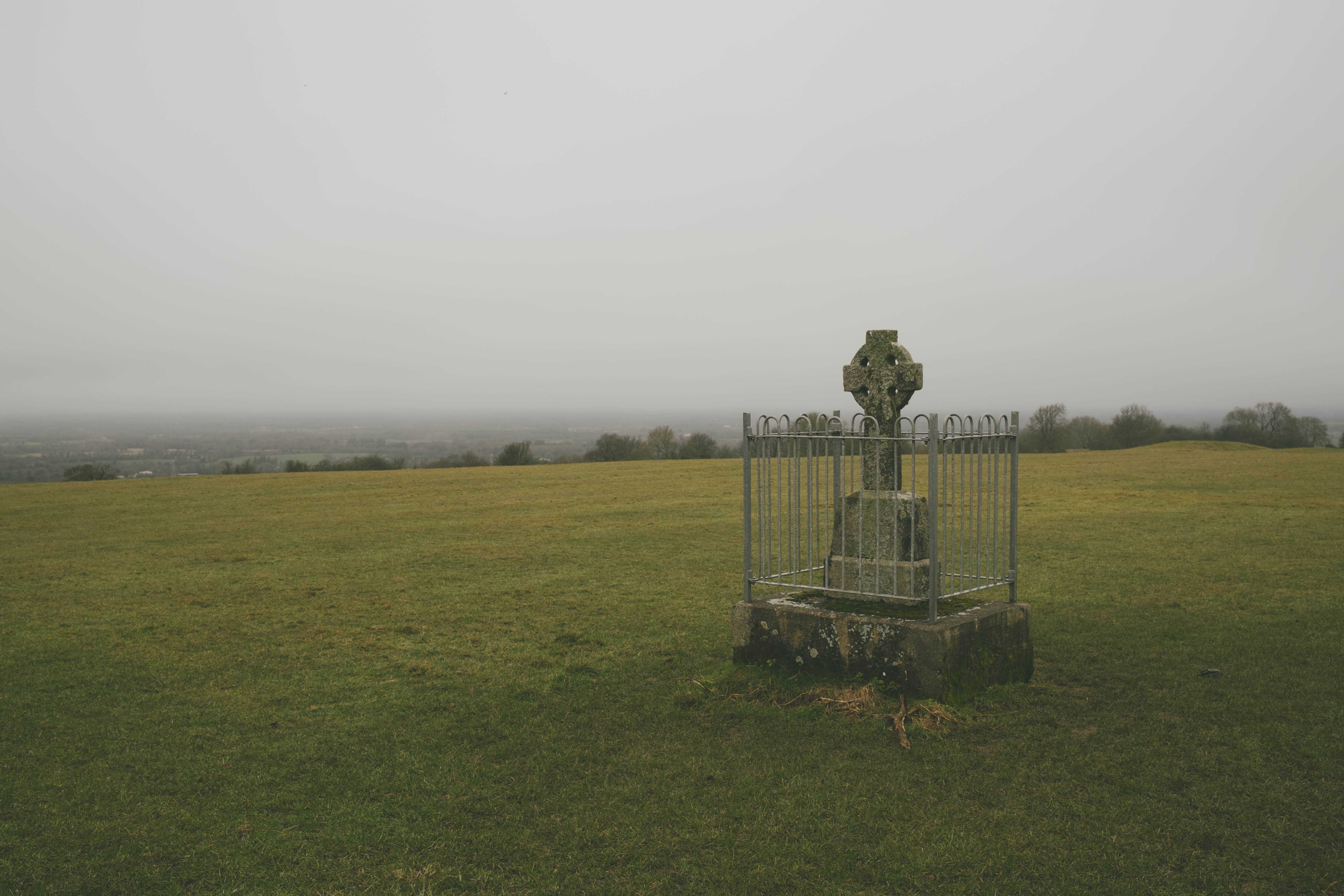 A grave stone with celtic cross in a large, empty field on a foggy day.
