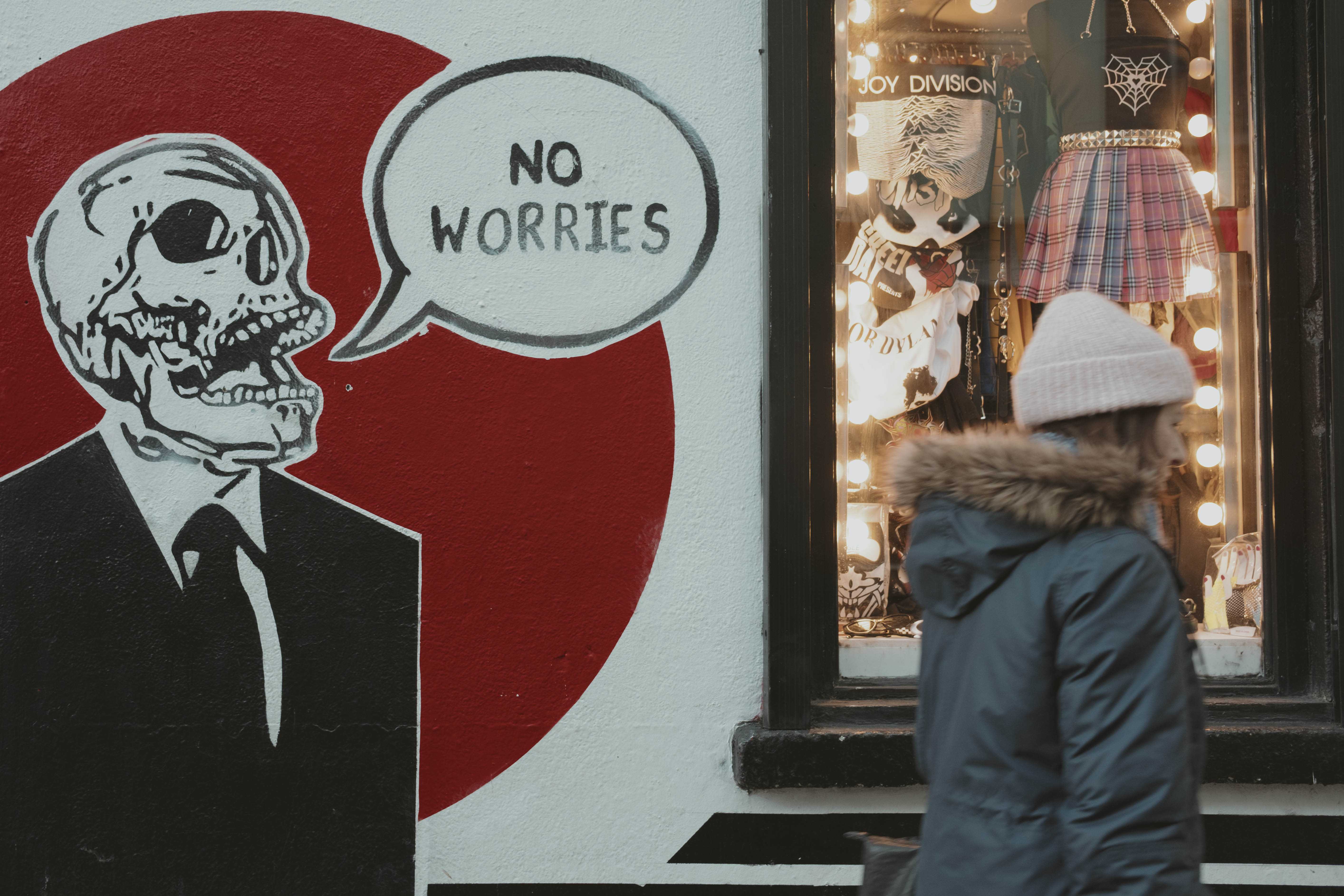 Street art with a skeleton in a suit saying 'No worries!' while a woman hurries by.