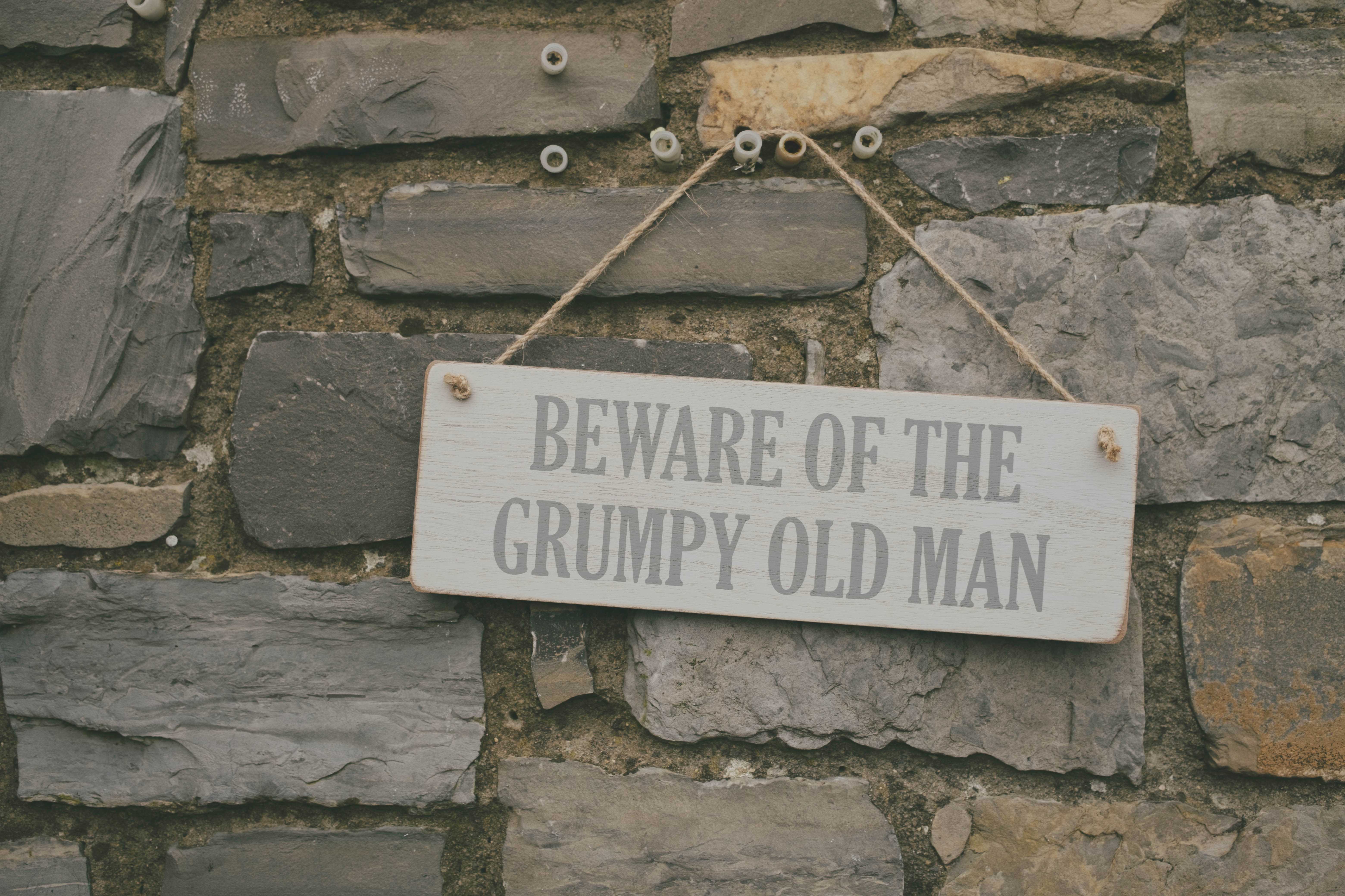 Sign on a stone wall that reads 'beware of the grumpy old man'