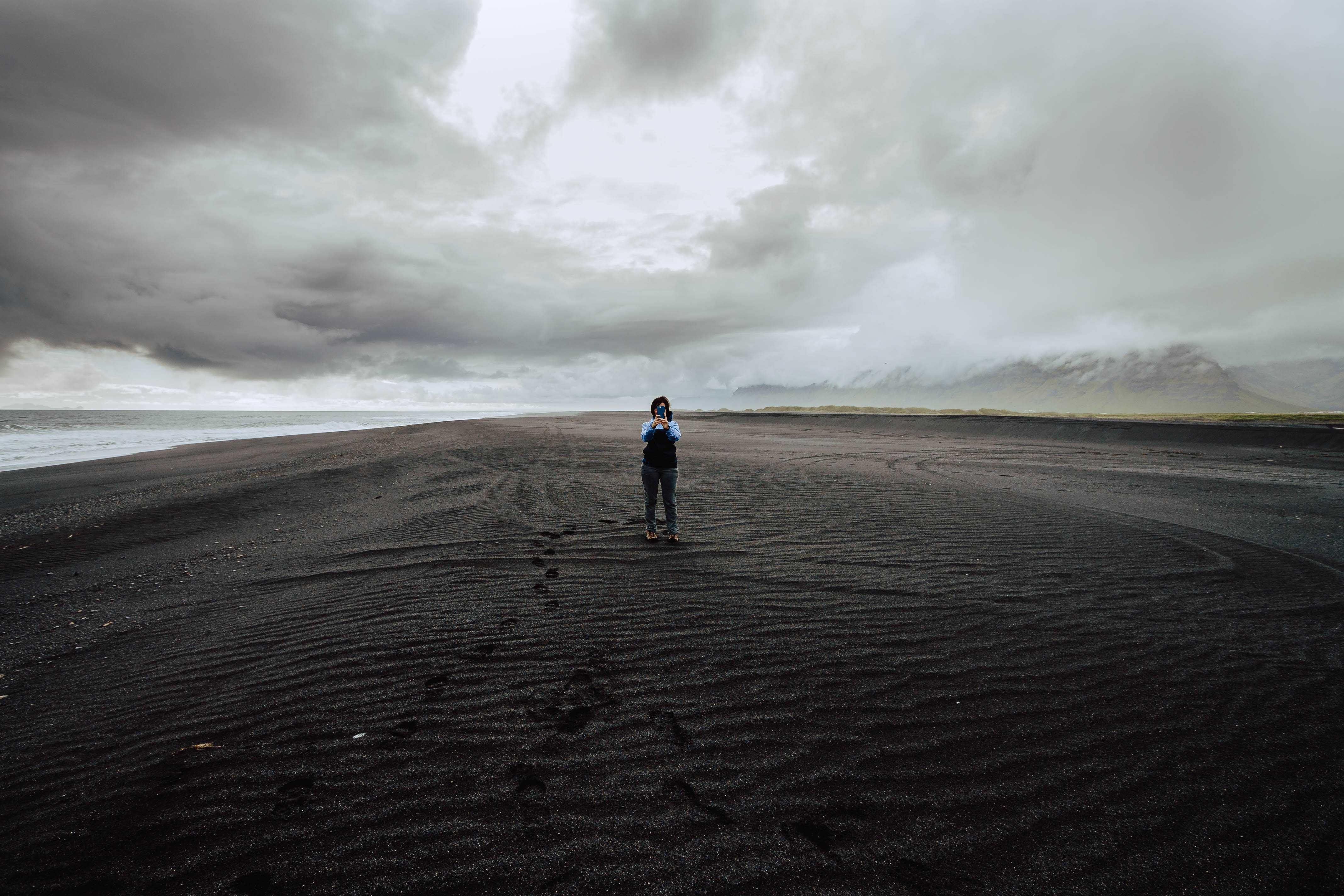 Mirna taking a photo of the photographer, wide shot, on a vast black sand beach