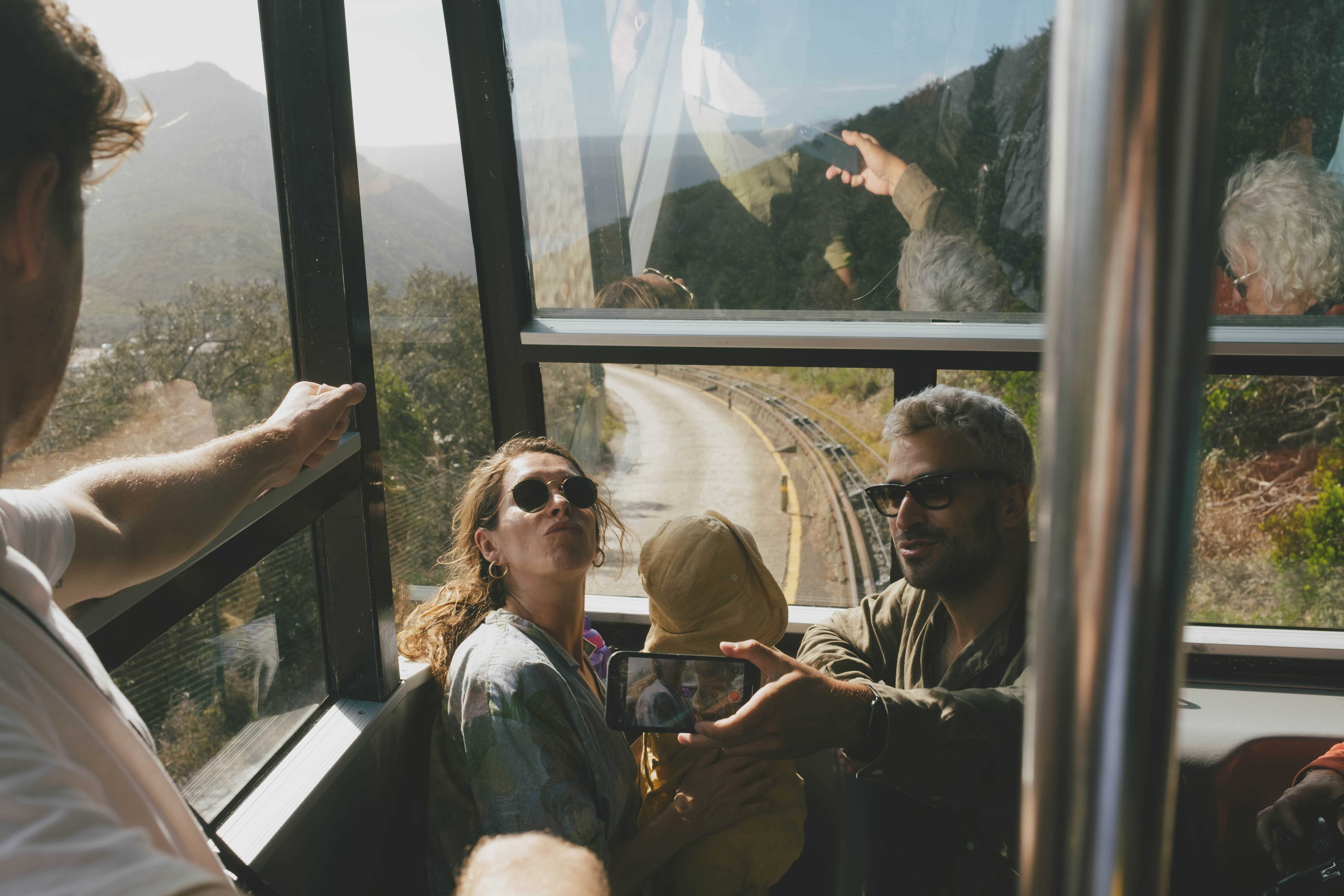 A family, husband, wife, and child, sitting in the front of a funicular posing for a selfie. Their reflections are in the glass.