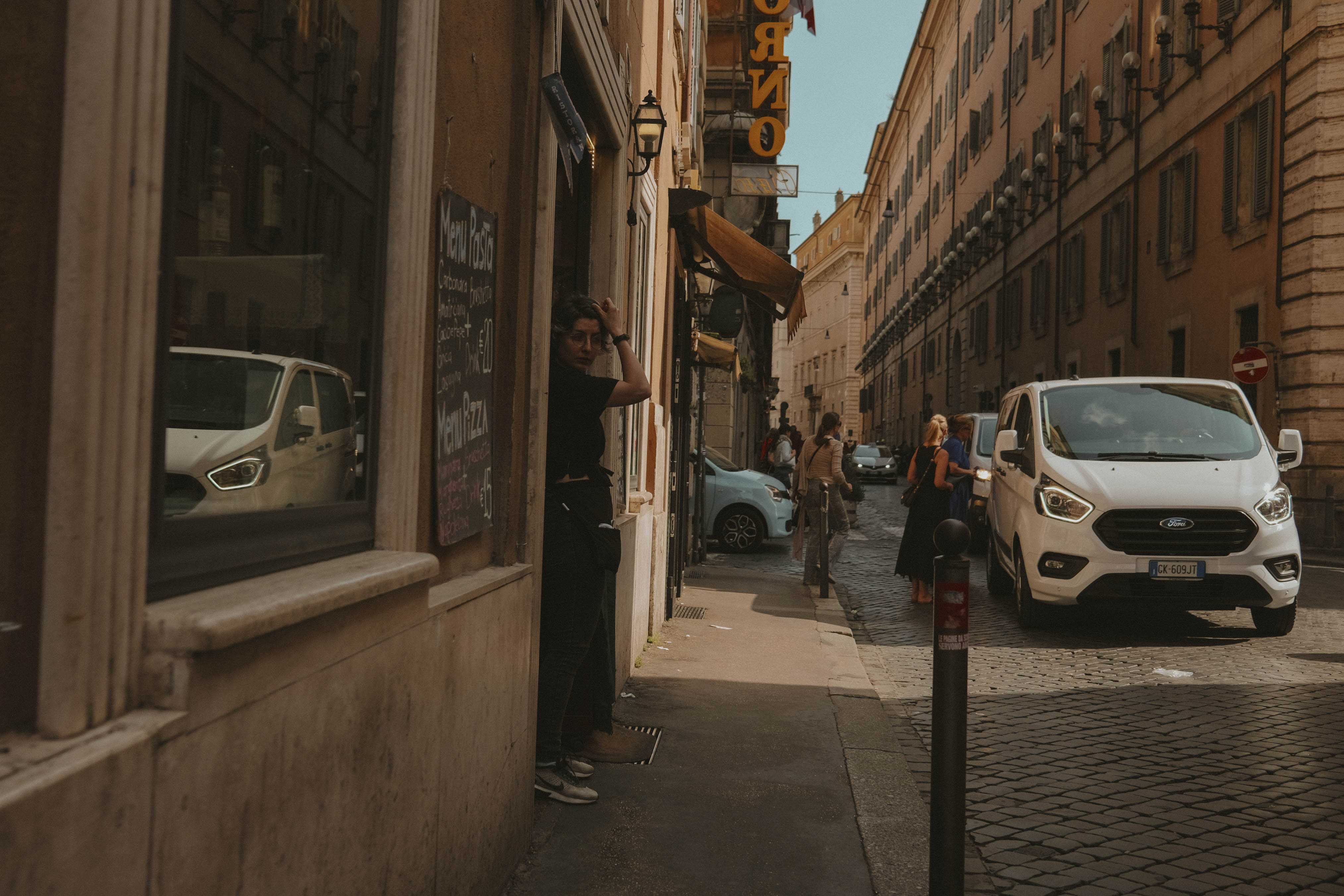 Woman standing at the entrance for a restaurant. A car is reflected in the window