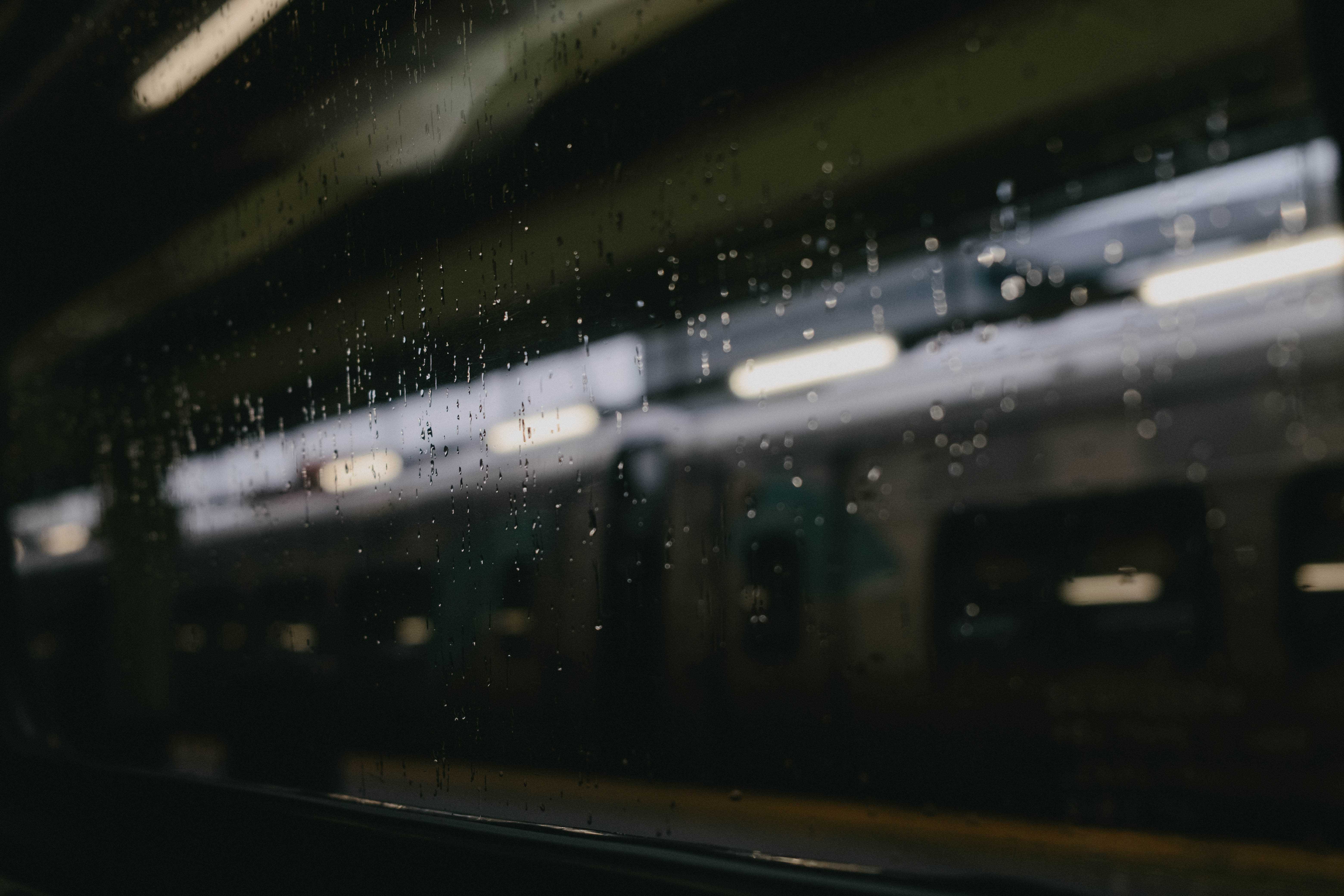 Shallow depth of field from inside a train, looking out the window. Streaks of rain are in focus while everthing else outside the window is blurred.